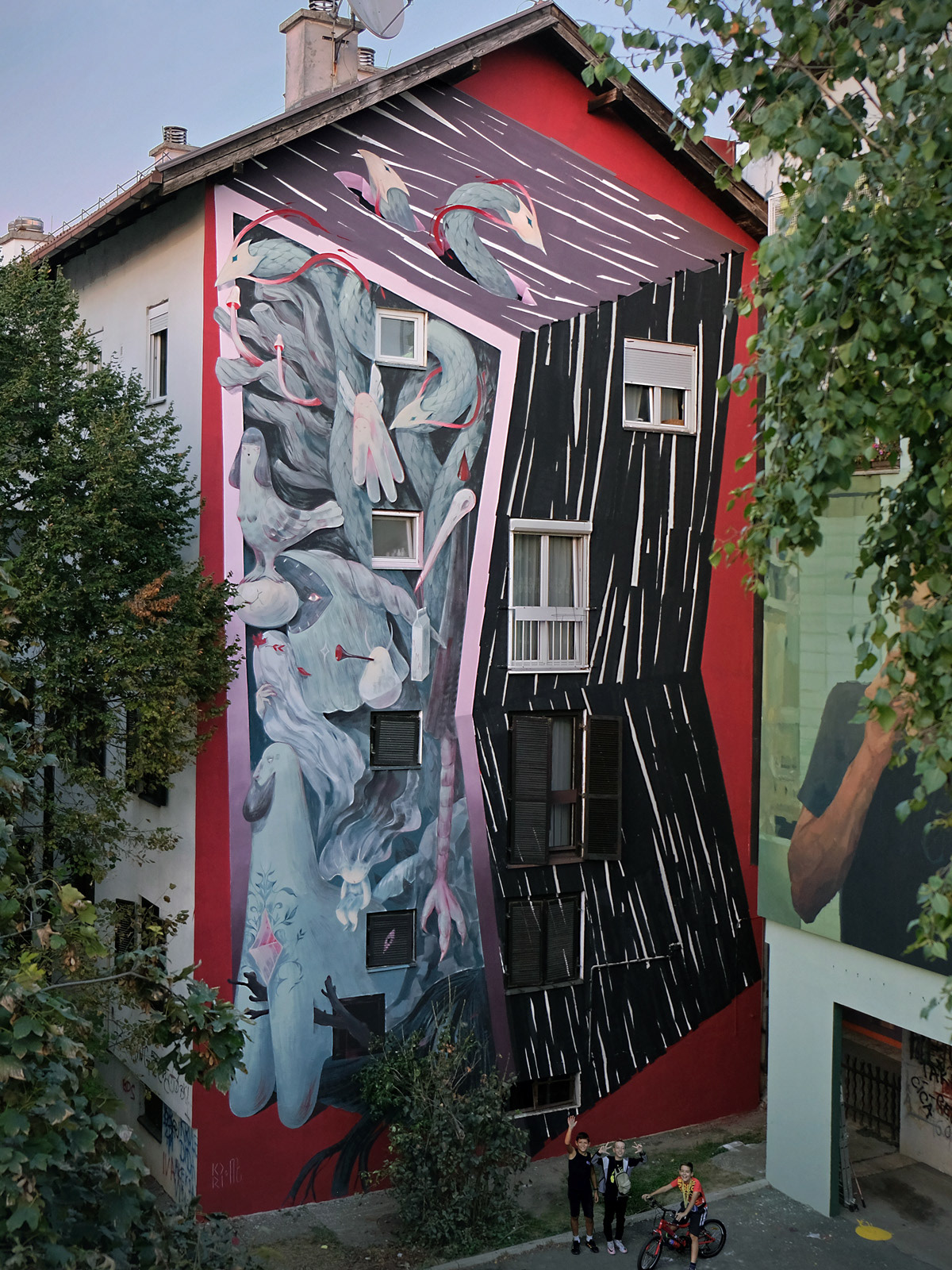 A tall mural on the end of a residential building depicting an abstract architectural shape and figures crowded inside of it.