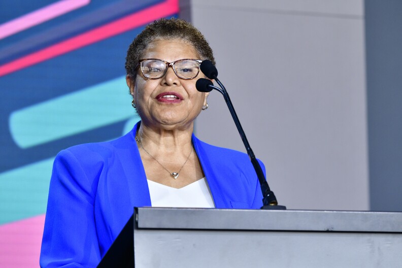 A close-up shot of Mayor Karen Bass in a bright blue suit at a podium with a microphone. 