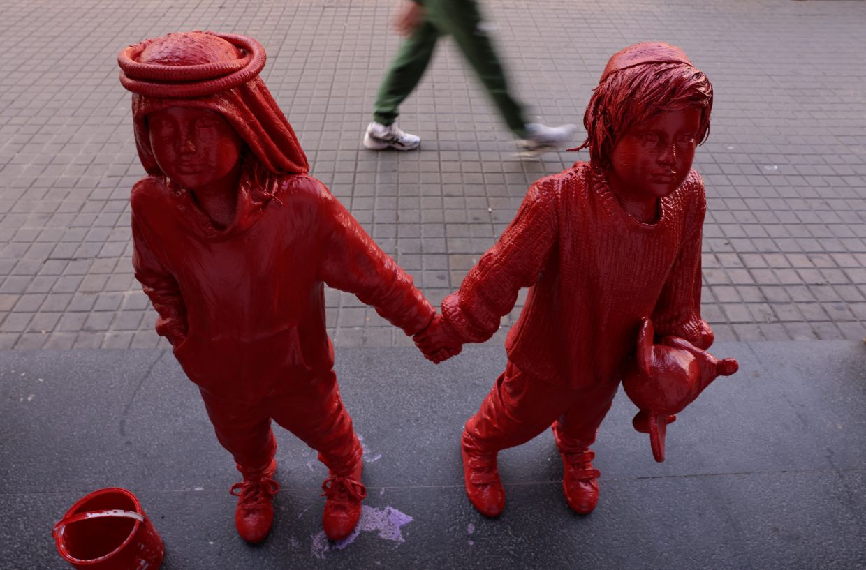 A pedestrian at Las Ramblas in Barcelona walks past life-size statues of an installation entitled 'The Children Of Peace', created by Colomina and representing the hope of the Israeli-Palestinian conflict. Photo: Reuters