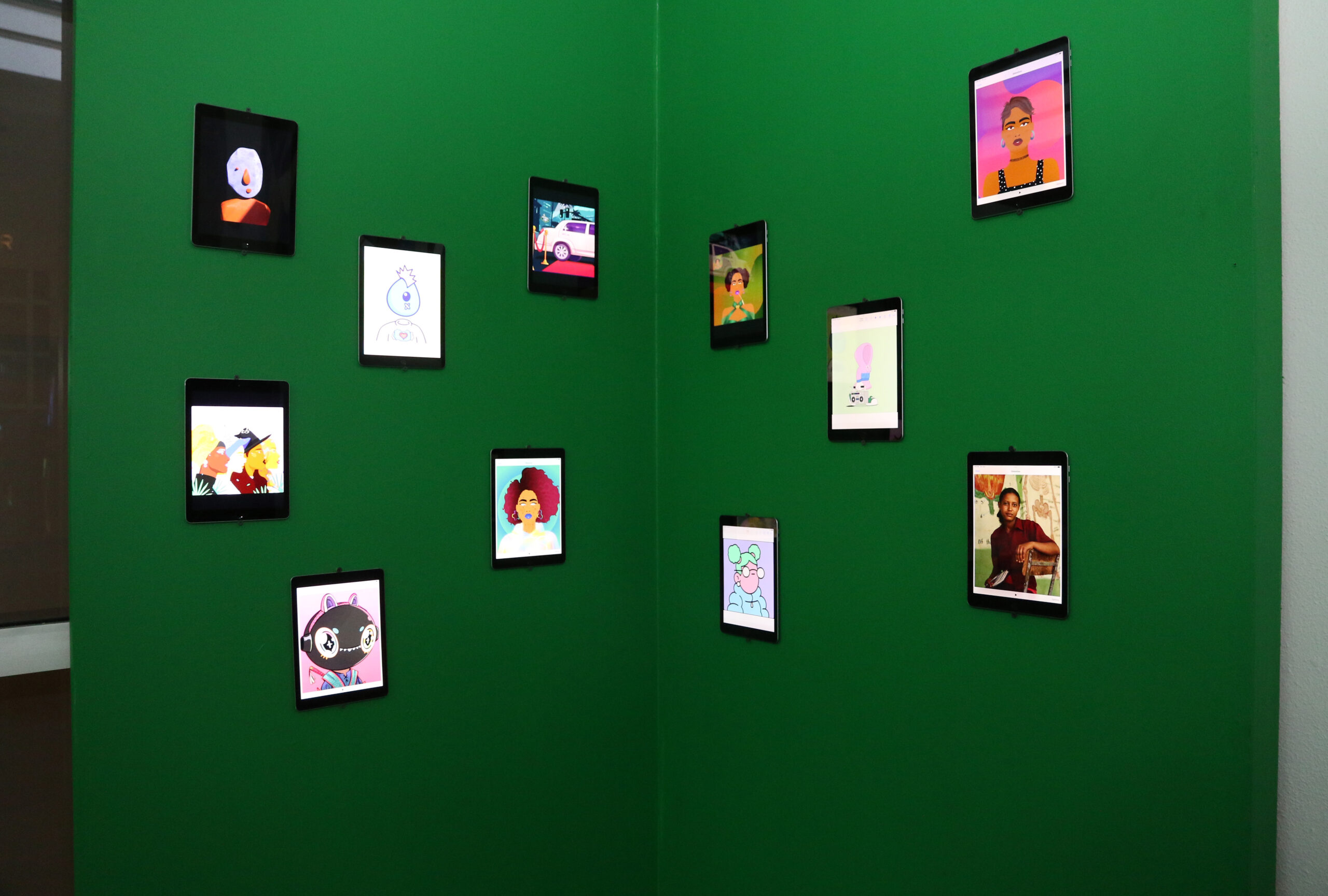 IPads displaying NFTs hang on green wall.