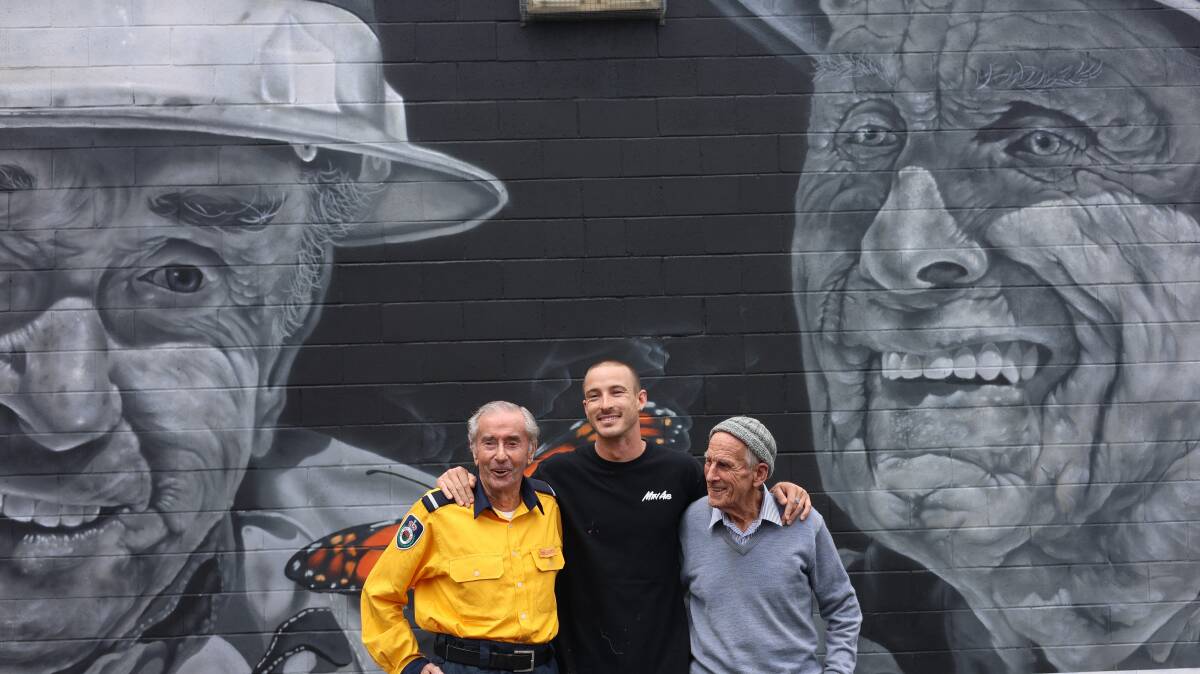 Kiama street artist Samuel Hall with his latest mural and the two volunteer firefighters, Brian Coates and John Matters, who were the subject of the artwork. Picture by Erin Olafson