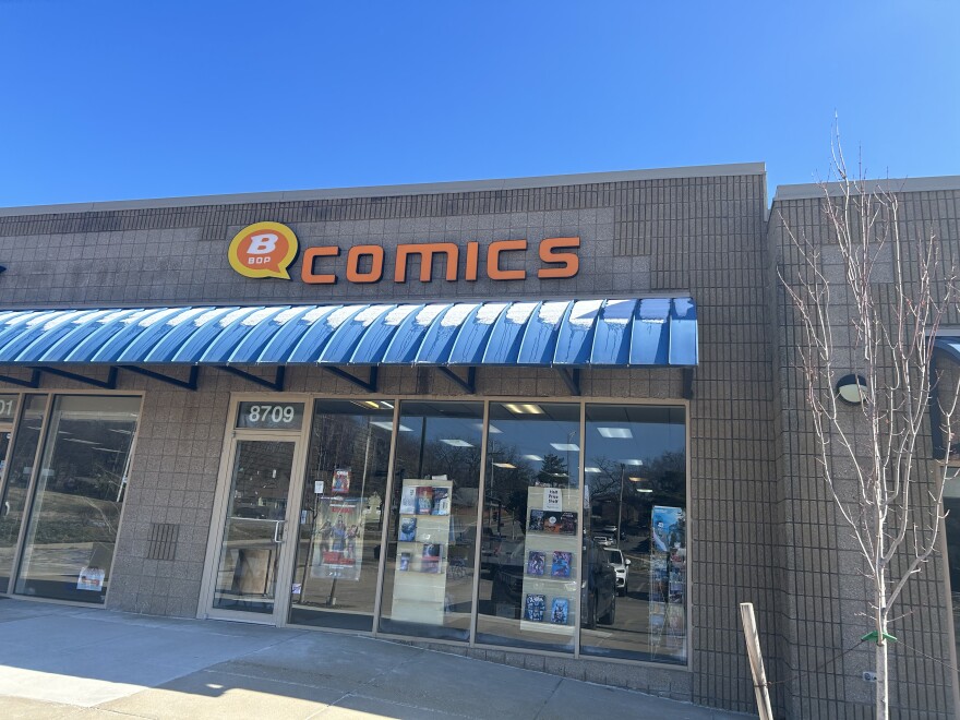 Exterior view of B-Bop Comics in a brown brick building with blue awning and orange sign. 