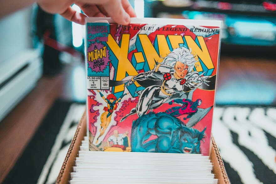A hand pulls an X-Men comic upward out of a cardboard box.