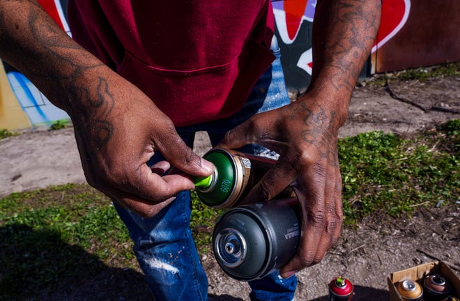 Indianapolis street artist Kwazar Martin swaps spray nozzles Monday, March 11, 2024, while putting the finishing touches on his most recent work, a graffiti mural of Iowa Hawkeyes basketball player Caitlin Clark.