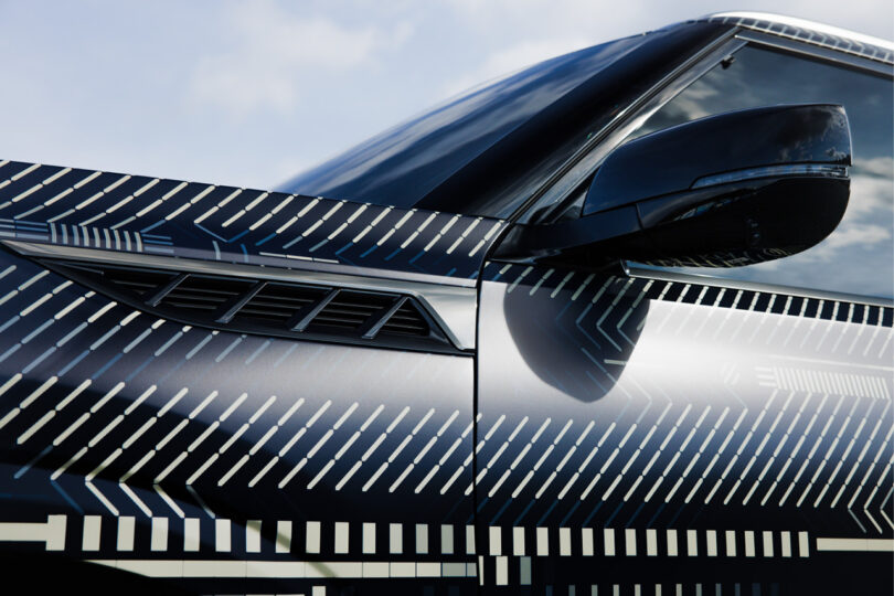 Front driver's side section of the new Infiniti GX80 wrapped in a monochromatic dash and square pattern designed by digital artist Kaoru Tanaka
