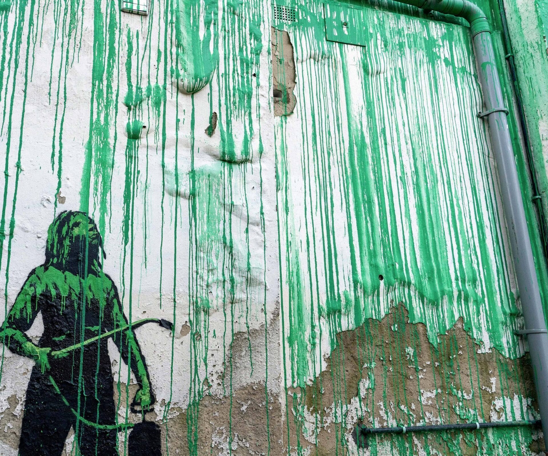 A detail of a new Banksy mural all in green and black paint, featuring a caveman-like figure under drips of green paint.