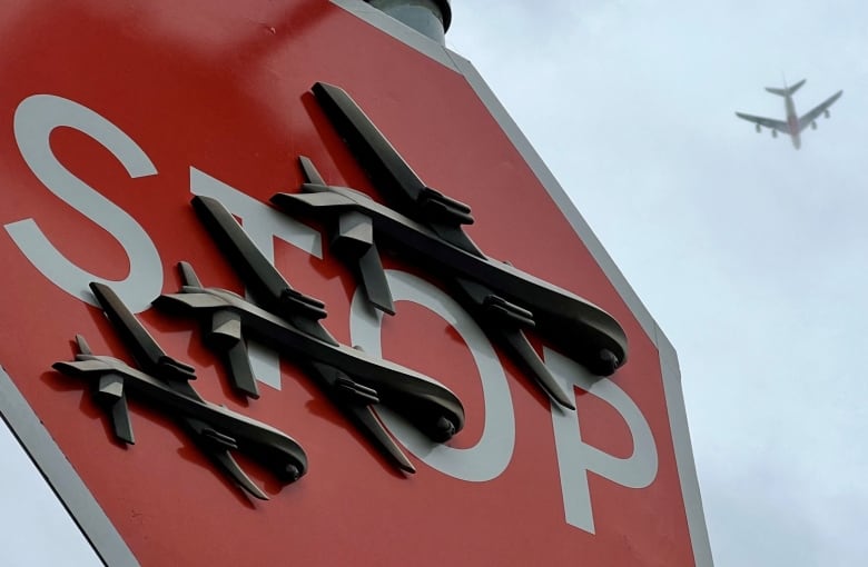 A stop sign adorned with artwork depicting military drones is seen.
