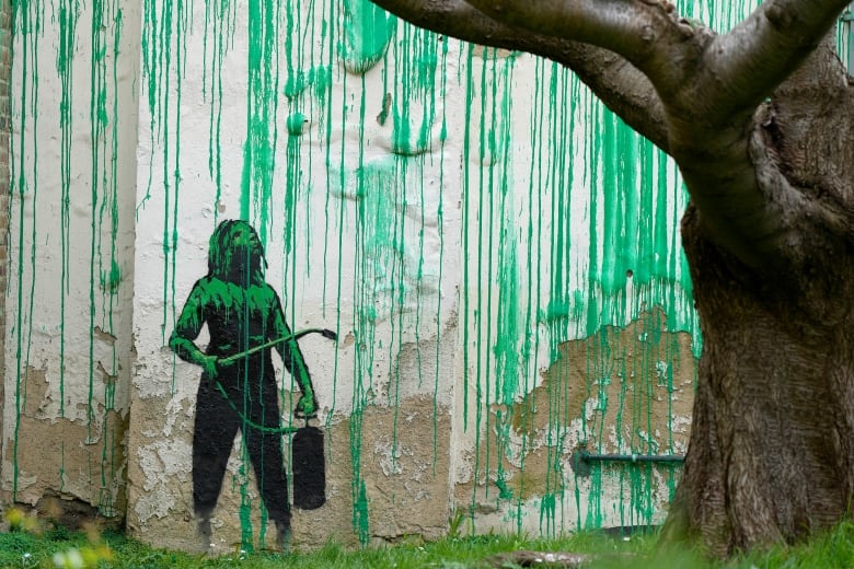 A mural on the side of a building shows a girl holding a pressure washer, surrounded by green drips