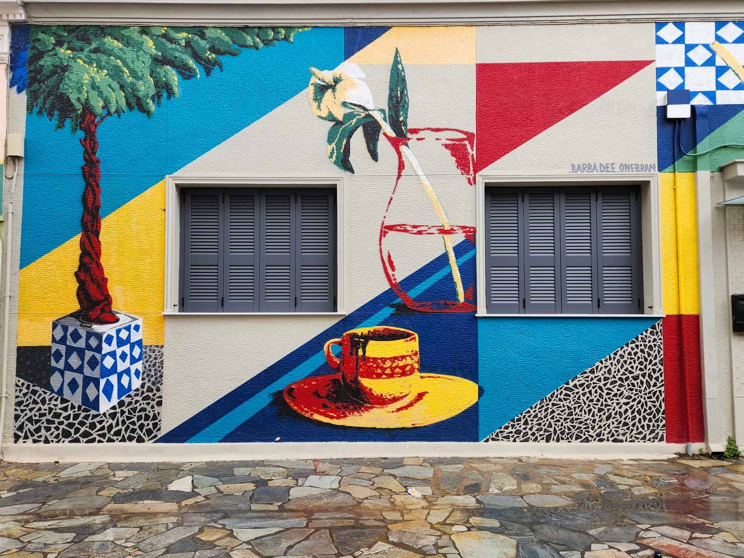 Brightly coloured street art of a tree, coffee cup and flower in a vase as well as geometric patterns on a house in Athens - my street art tour of Athens review