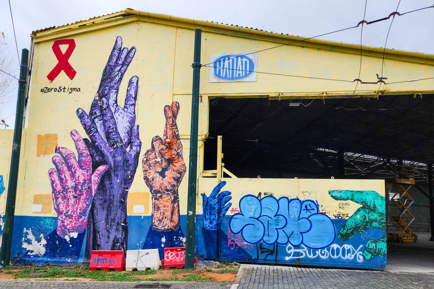 View of the old bus garage in Athens with orange, pink and purple hands and a red AIDS awareness ribbon - one of the artworks we saw on a street art tour of Athens with kids