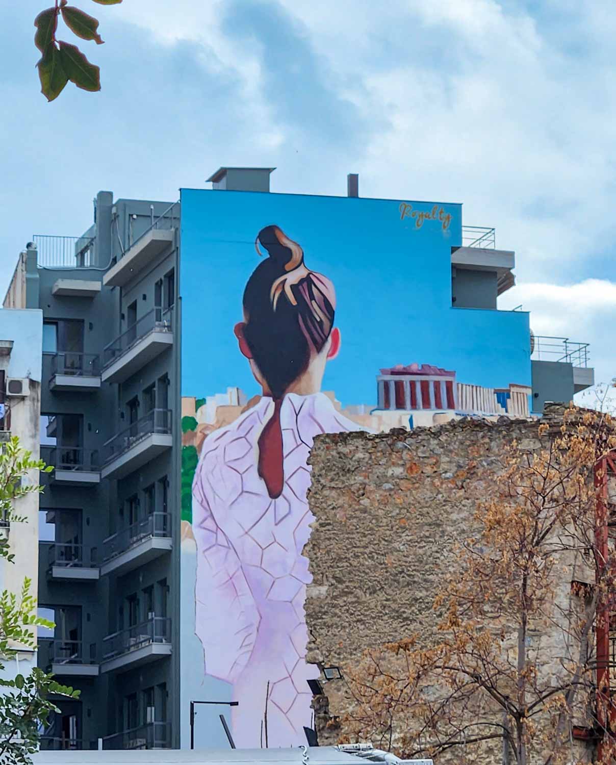 View of a girl in a dress painted on the side of a multistorey block of flats, seen during our street art tour of Athens with kids