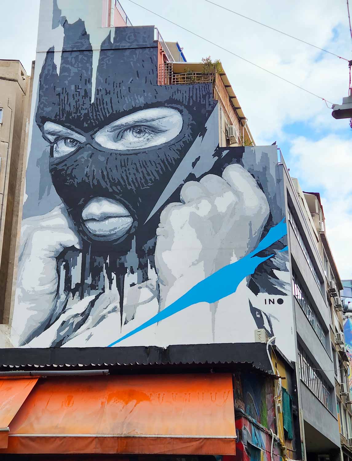 Piece of street art by INO in Athens of a person in a black mask on the side of a building, spotted on our street art tour of Athens with kids