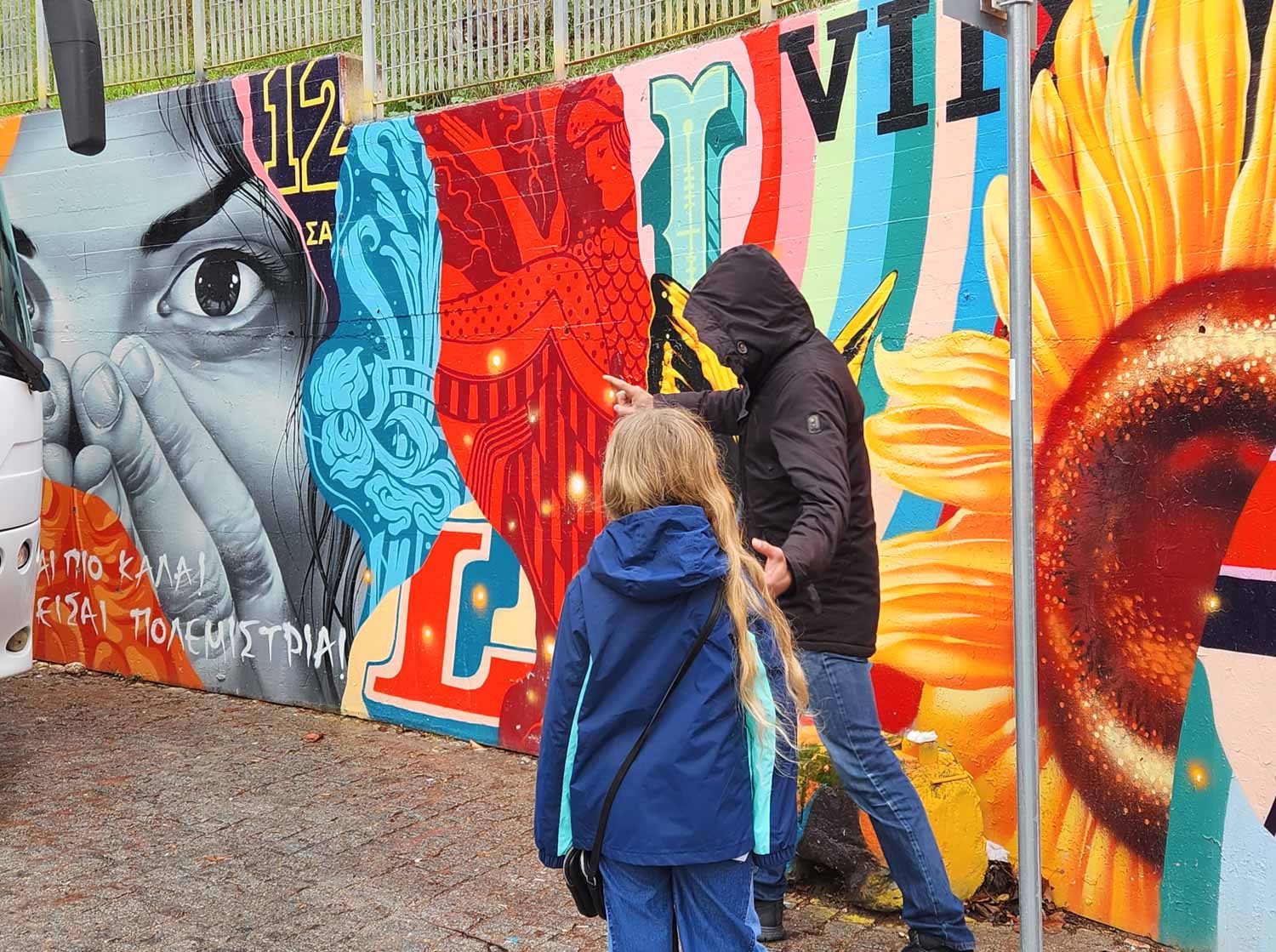 My daughter with our tour guide Nikos looking at a brightly coloured mural including a sunflower and a woman's face - my review of a street art tour of Athens with kids