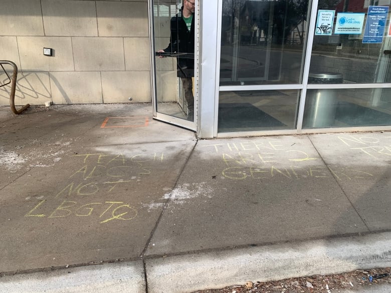 Offensive phrases written in yellow chalk outside library on damp sidewalk.