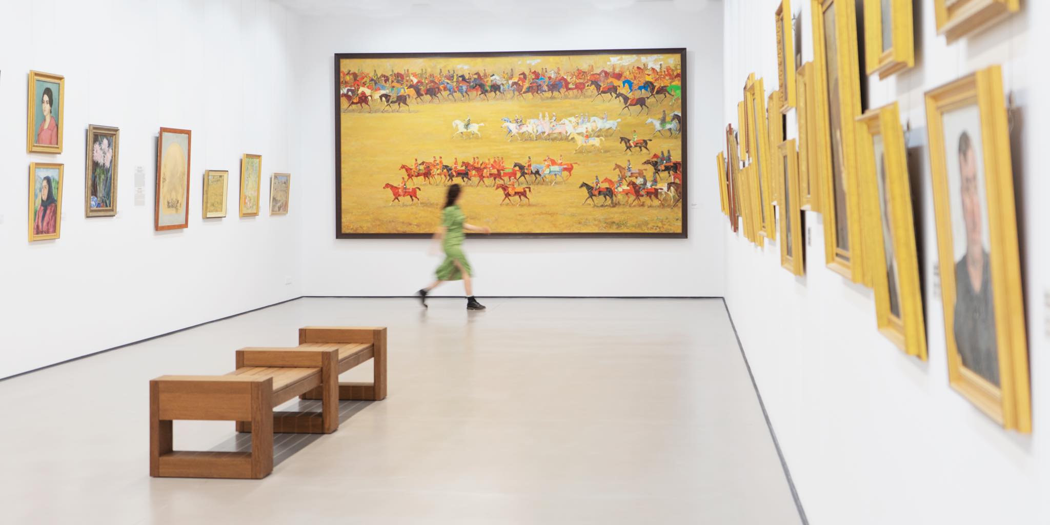 The interior of an art gallery with large yellow paintings on the wall and a woman walking through