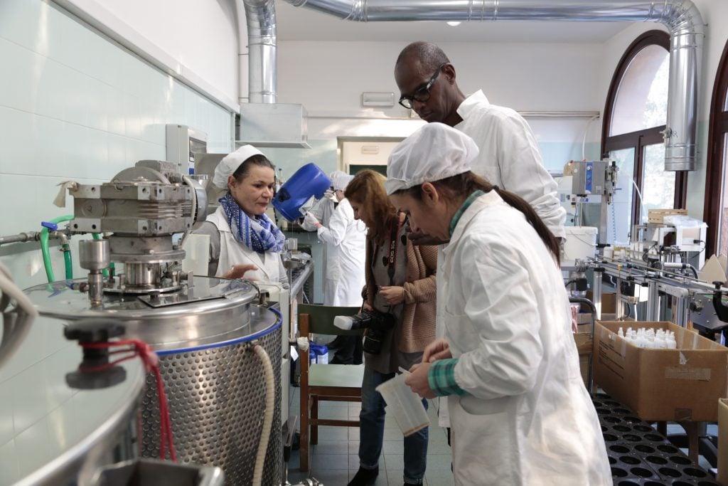 The women of Giudecca prison in labcoats working with equipment, while the U.S. artist Mark Bradford observes.