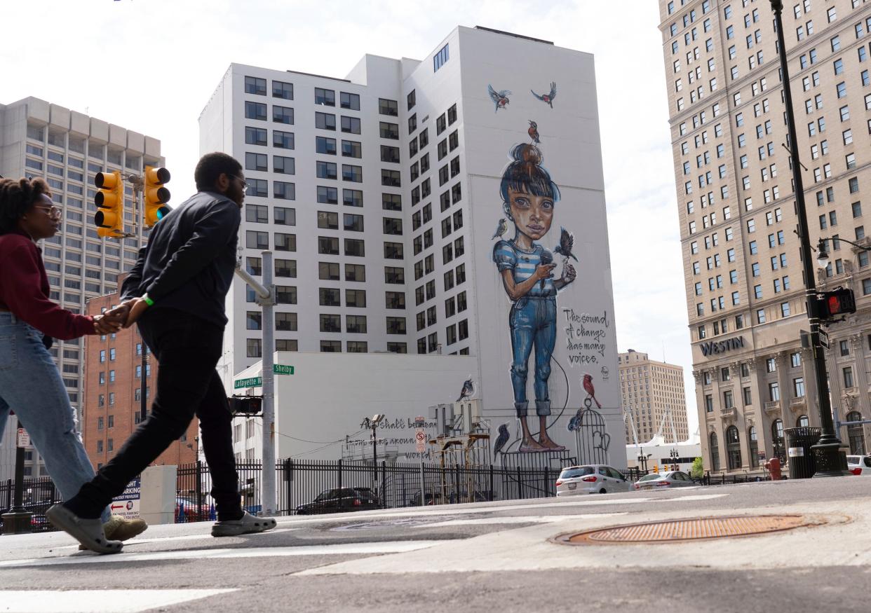 People walk past a large mural near along West Lafayette Boulevard and Shelby Street in downtown Detroit on Monday, June 10, 2024.